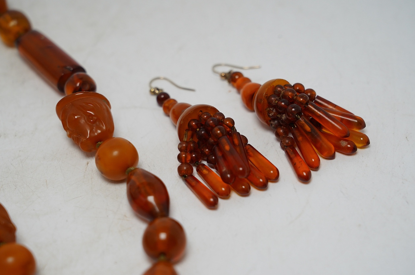 Two amber bead necklaces including Chinese with carved busts, 76cm and a pair of drop earrings, gross weight 145 grams. Condition - poor to fair